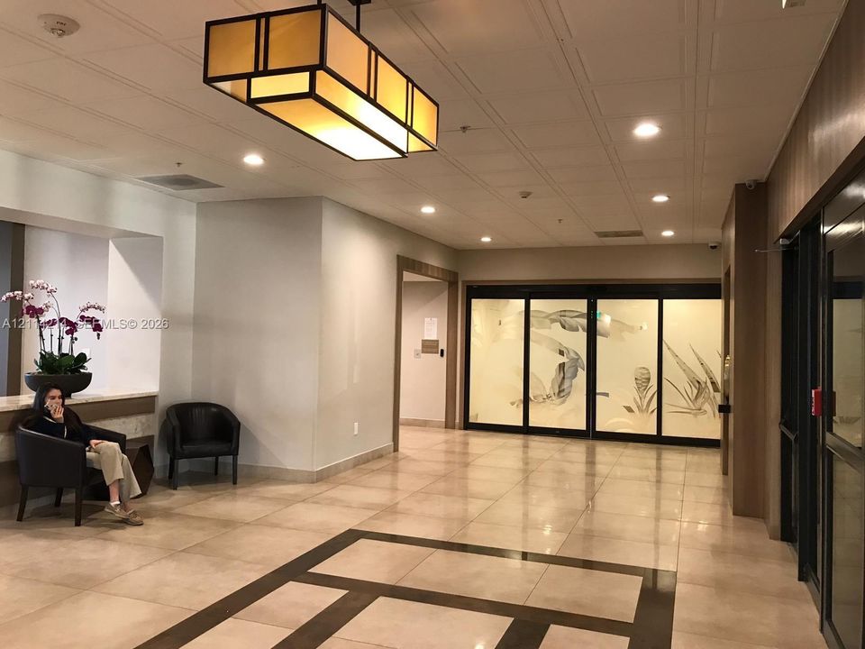 Lobby featuring large-format tile flooring with inlaid geometric borders, rectangular pendant lighting, and decorative frosted glass panels with etched leaf motifs