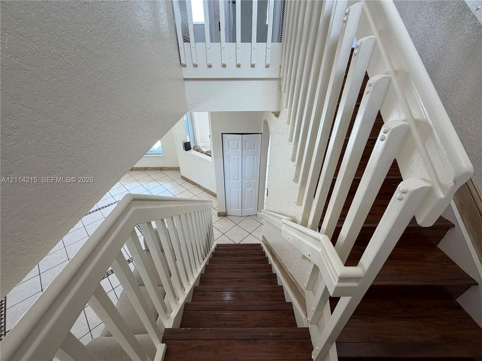 Staircase featuring wood-finish treads and white balusters with matching handrails, complemented by ceramic tile flooring and white bi-fold closet doors
