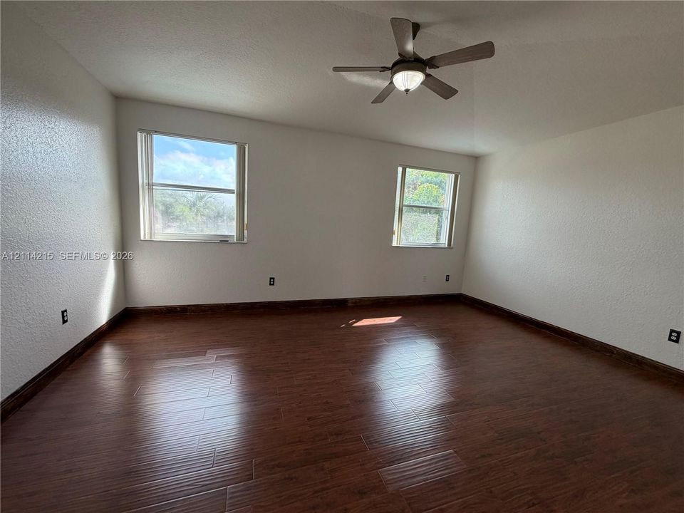 Spacious room featuring wood-finish flooring, neutral wall tones, two windows, and a ceiling fan with integrated lighting