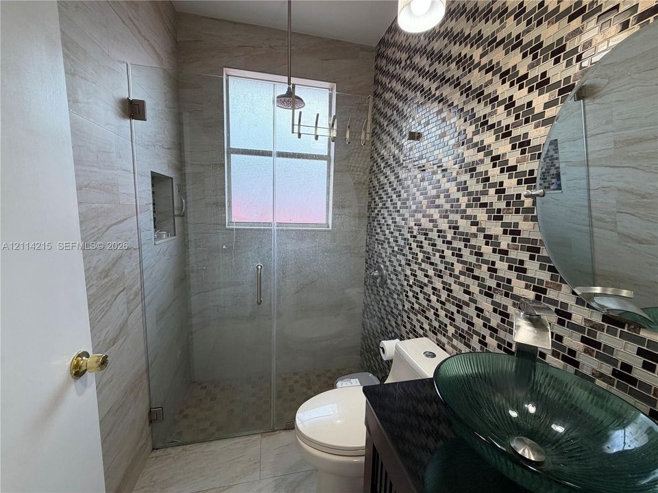 Bathroom featuring a glass vessel sink, dark stone countertop, mosaic tile accent wall, and a walk-in shower with a glass enclosure and recessed niche