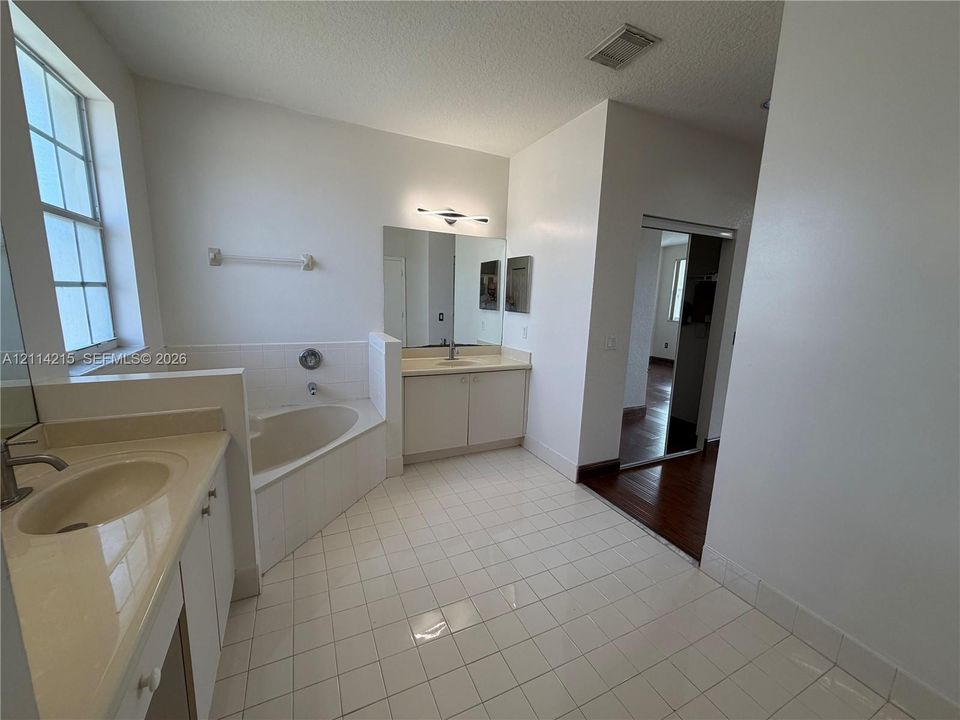Bathroom featuring a soaking tub, dual-sink vanity with light-tone countertops, polished wall-mounted mirrors, and white ceramic tile flooring