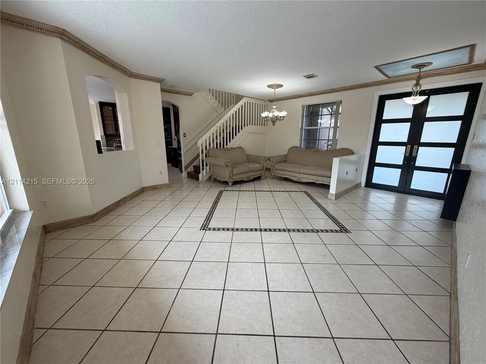 Interior space featuring diagonal tile flooring with decorative inlay, double-entry door with frosted glass panes, staircase with vertical balusters, and crown molding