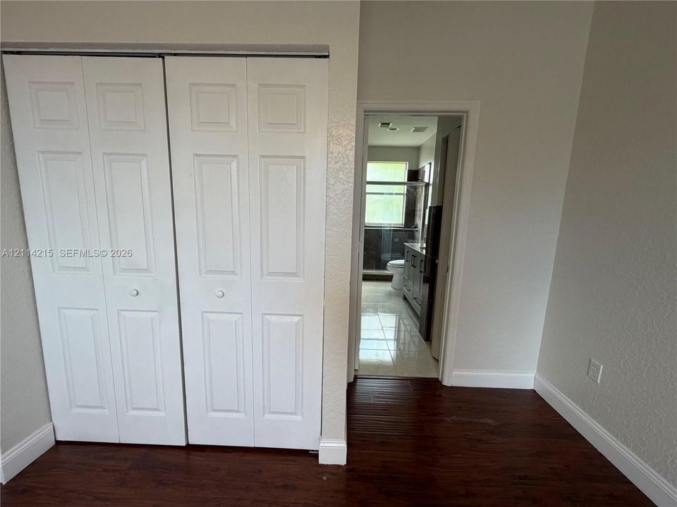 Interior space featuring wood-finish flooring, white bi-fold closet doors, and tile flooring visible in the secondary area