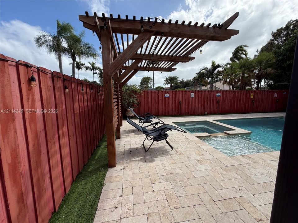 Outdoor area featuring a built-in wooden pergola, stone paver decking, a swimming pool with an integrated spa, and a vertical wood privacy fence