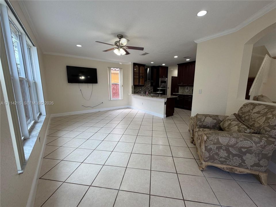 Open concept area featuring large-format ceramic tile flooring, recessed lighting, a ceiling fan, and dark-toned cabinetry with a stone-surfaced breakfast bar