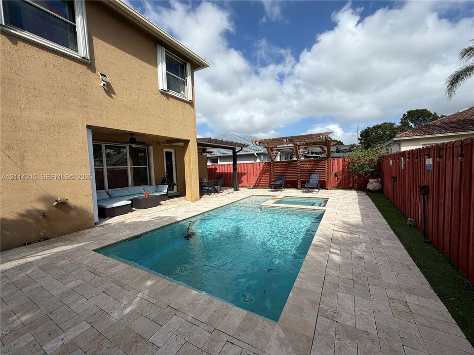 Backyard area featuring an in-ground swimming pool with an integrated spa, stone paver decking, a covered patio, and a wooden pergola