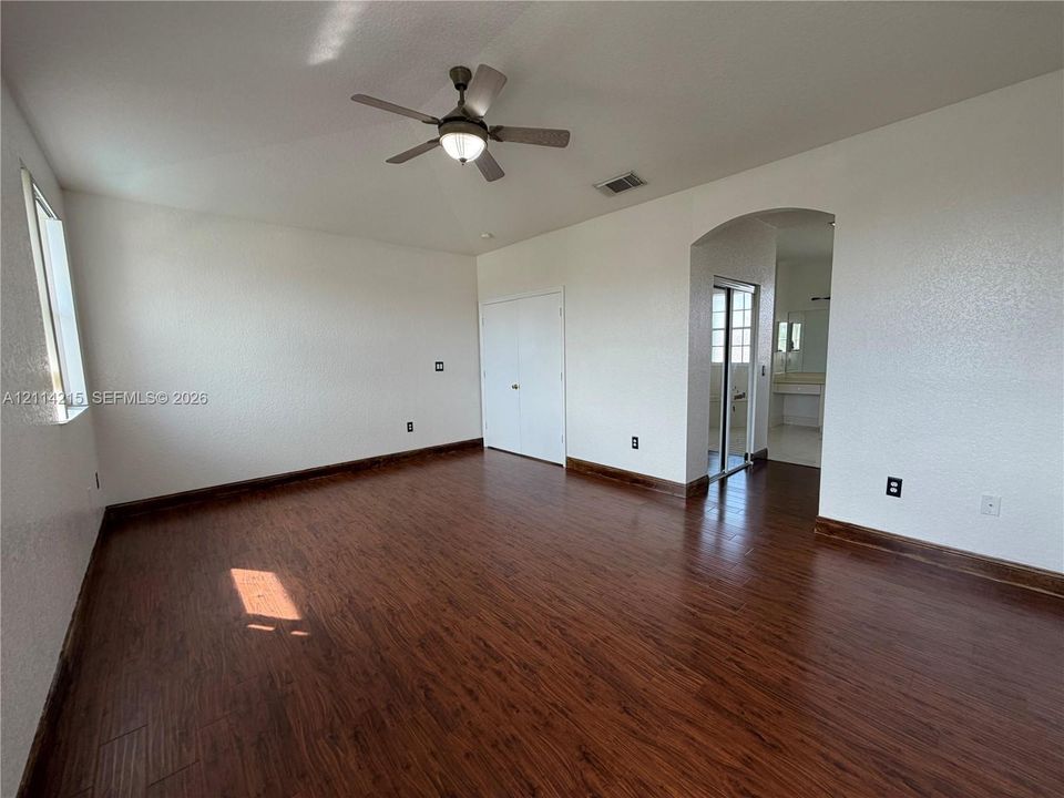 Spacious room featuring wood-finish flooring, vaulted ceilings, and an overhead ceiling fan