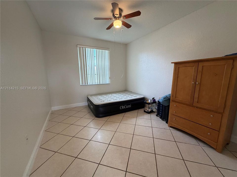 Room featuring light-colored tile flooring, a neutral wall finish, and an integrated ceiling fan with light fixture