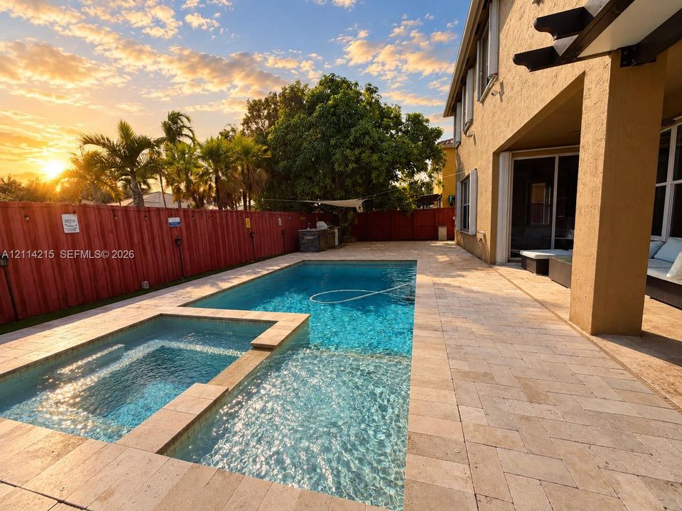 Rear exterior featuring a stone-paver patio, in-ground swimming pool, attached elevated spa, and a tall privacy fence