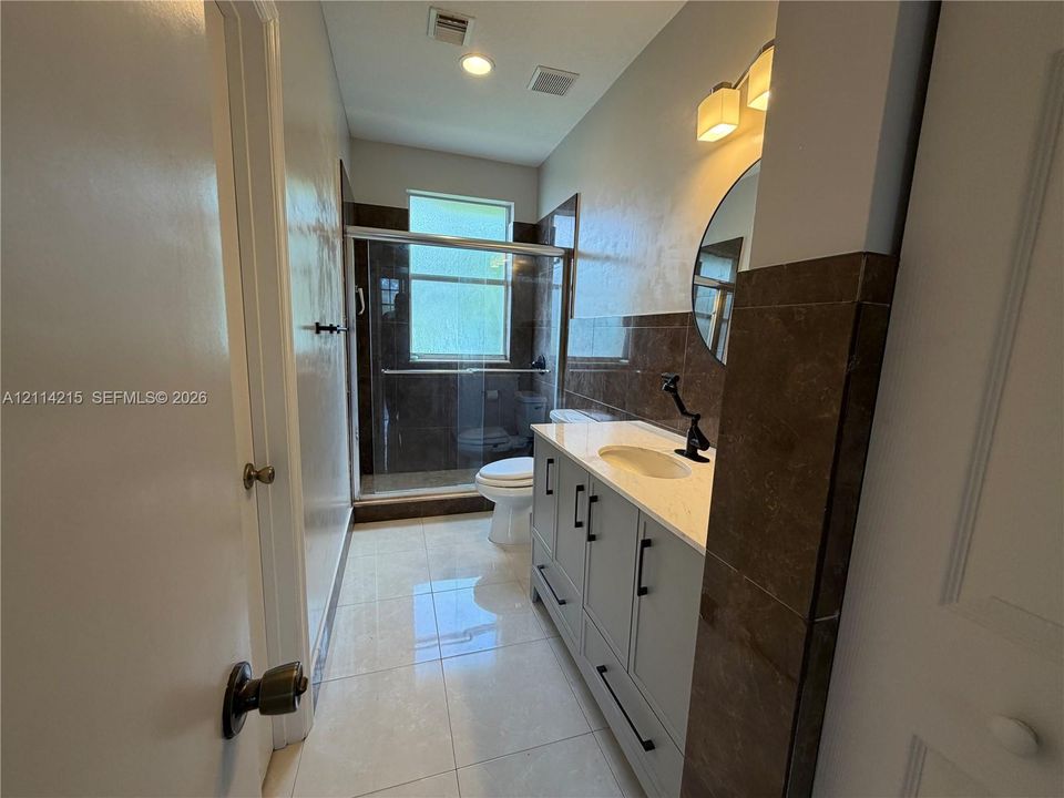 Bathroom featuring a vanity with a light-toned countertop, dark stone wall tiling, a walk-in shower with a glass enclosure, and large-format tile flooring