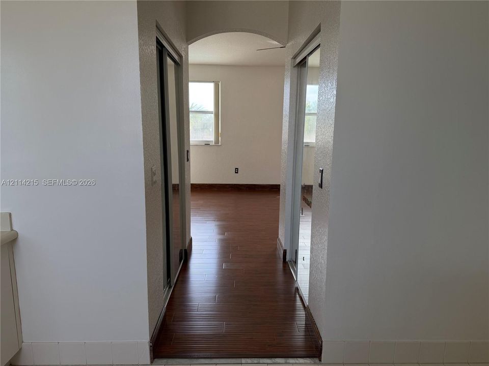 Arched hallway featuring wood-finish flooring and dual mirrored sliding closet doors
