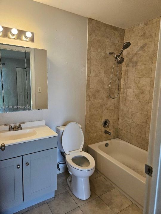 Bathroom featuring a vanity with an integrated sink, rectangular medicine cabinet, wall-mounted light fixture, and shower-tub combination with stone-finish tile surround and handheld shower head
