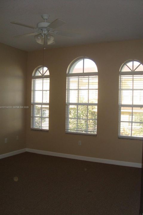 Three arched windows with horizontal blinds, neutral wall paint, and a white ceiling fan with integrated lighting