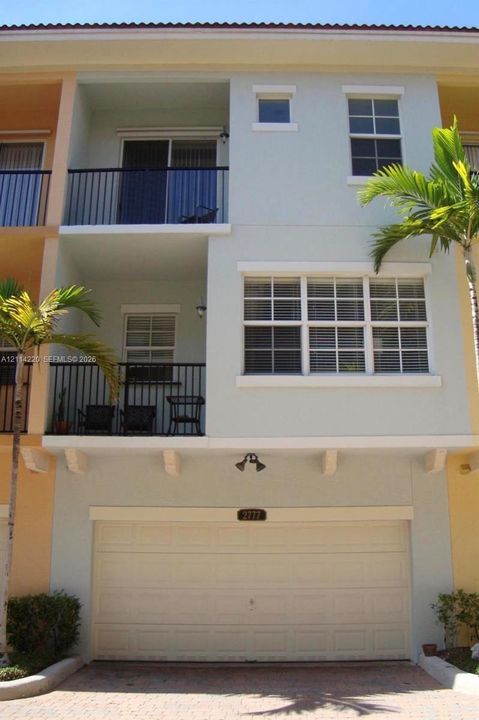 Multi-story residence featuring a two-car garage, dual private balconies with metal railings, and multi-pane windows