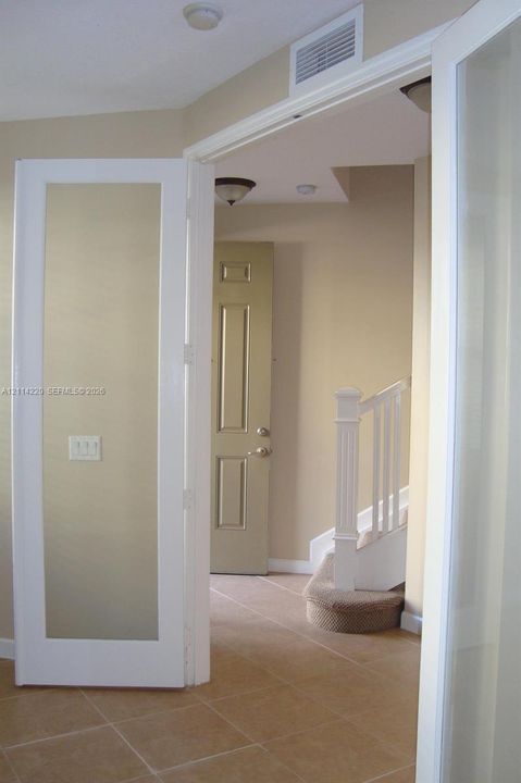 French-style doors with glass paneling, tile flooring, staircase with white railing, and paneled interior door