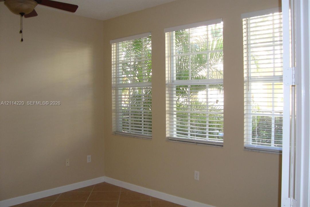 Neutral interior featuring tile flooring, three large windows with horizontal blinds, and a ceiling fan with integrated lighting