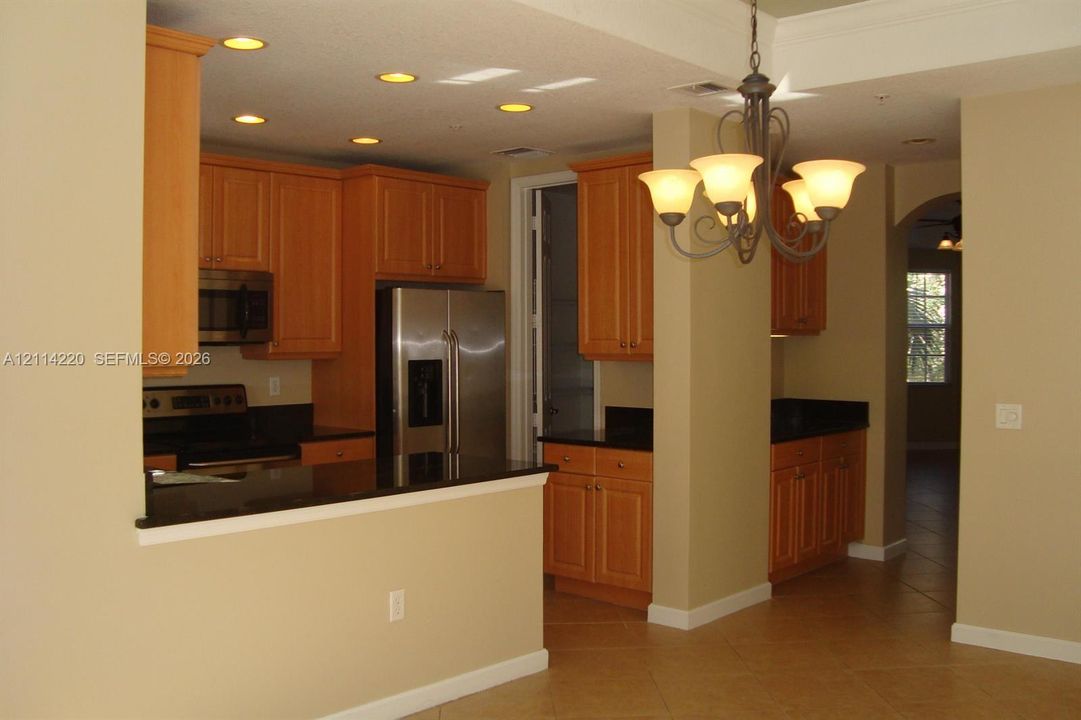 Kitchen featuring light-finish cabinetry, dark solid-surface countertops, stainless steel appliances, recessed ceiling lighting, and a multi-arm chandelier