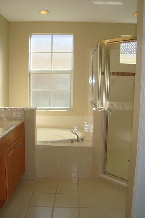Bathroom featuring a tiled soaking tub deck, a separate glass-enclosed shower, wood-finish cabinetry, ceramic tile flooring, and a multi-pane window