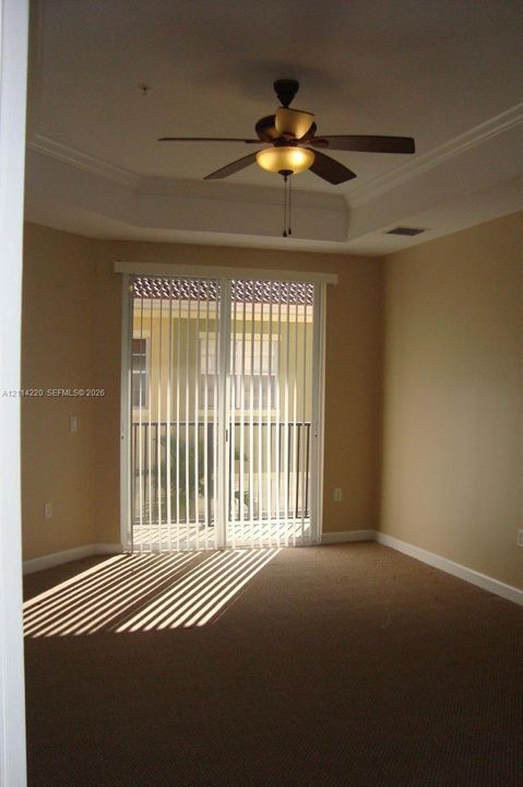 Room featuring a tray ceiling, ceiling fan with integrated lighting, and sliding glass doors with vertical blinds