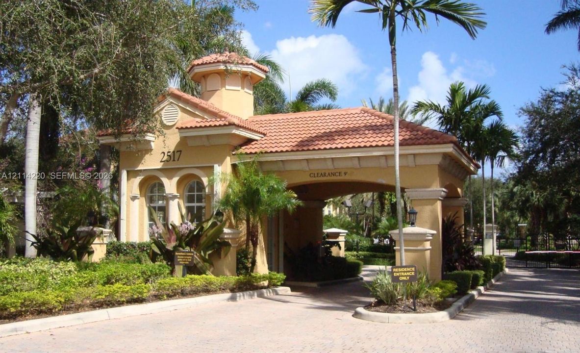 Gated entrance featuring a terracotta tile roof, stucco exterior, architectural cupola, arched window detailing, and paver driveway