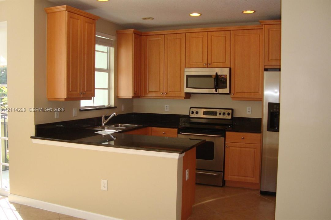 Kitchen featuring wood cabinetry, dark stone countertops, stainless steel appliances, and recessed lighting