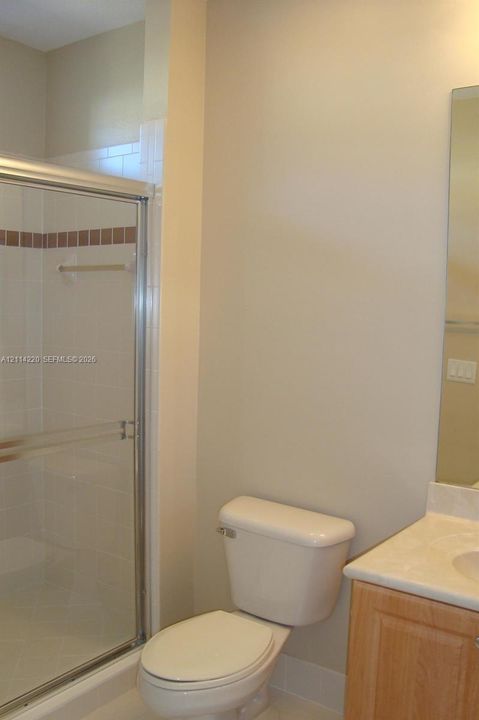 Shower enclosure with tile surround and inset decorative accent, wood-finish vanity cabinet, solid-surface countertop with integrated sink, and wall-mounted mirror