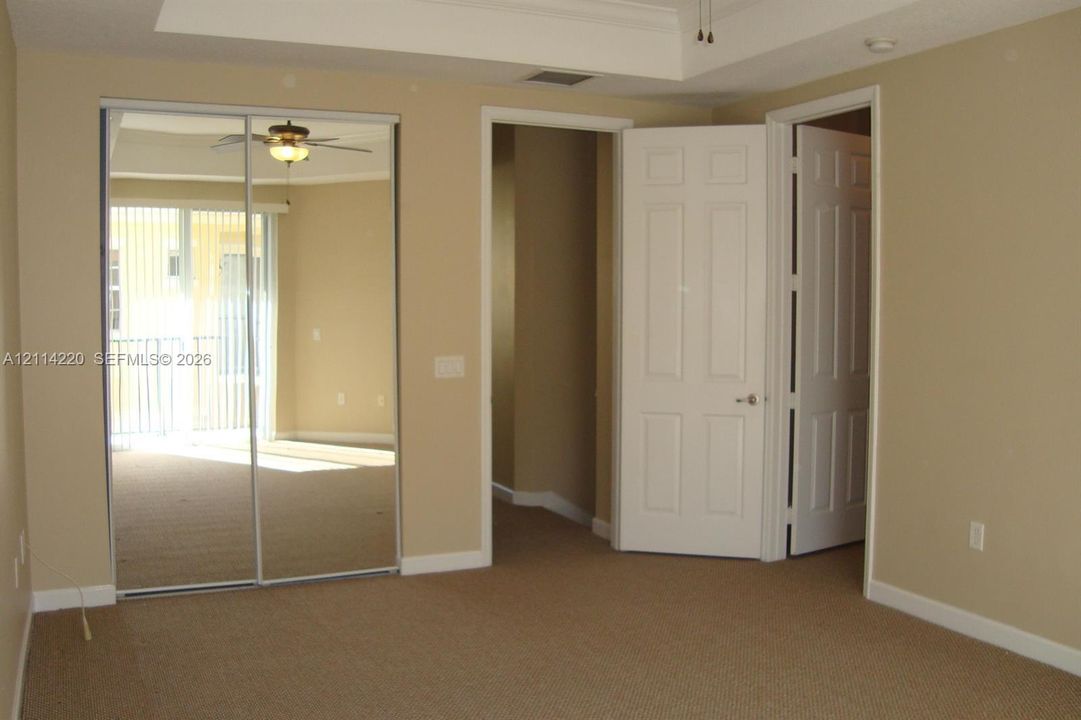 Neutral interior space featuring carpeting, tray ceiling, mirrored sliding closet doors, and six-panel interior doors