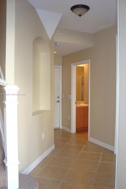 Neutral-toned interior featuring an arched wall niche, ceramic tile flooring, and a white architectural newel post with cap