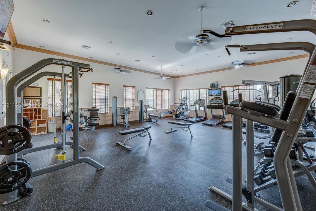 Spacious fitness center featuring rubberized flooring, recessed lighting, multiple ceiling fans, and built-in wood shelving