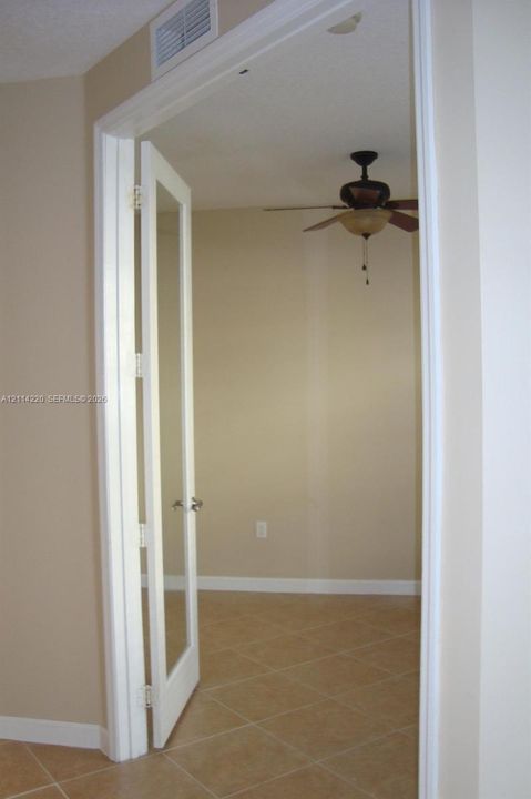 Double glass-pane doors featuring white frames, neutral tile flooring, and a ceiling fan with integrated lighting