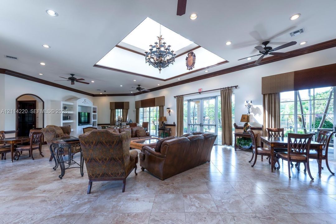 Large central skylight featuring an ornamental chandelier, stone-finish tile flooring, built-in cabinetry, crown molding, and recessed lighting