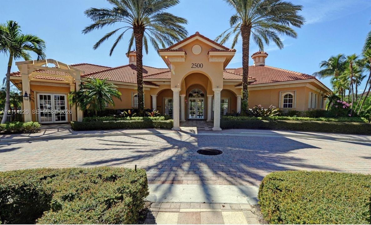 Mediterranean-style exterior featuring a terracotta tile roof, arched entryway with decorative columns, paver driveway, and manicured landscaping