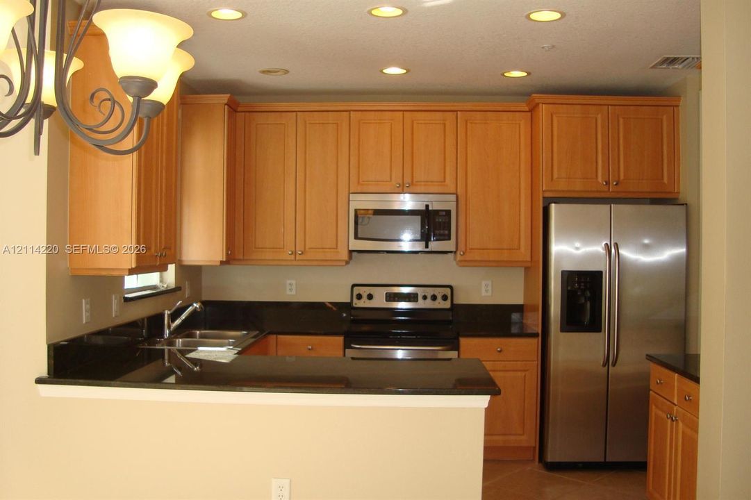 Kitchen featuring light wood-finish cabinetry, dark solid-surface countertops, built-in stainless steel microwave, stainless steel refrigerator, and recessed lighting
