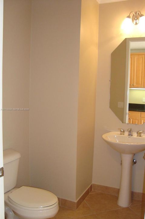 Pedestal sink with chrome faucet, beveled-edge wall mirror, ceramic tile flooring, and wall-mounted light fixture