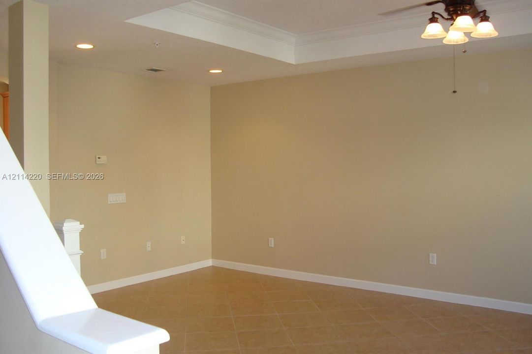 Interior space featuring a recessed tray ceiling, neutral wall tones, tile flooring, recessed lighting, and a multi-light ceiling fixture