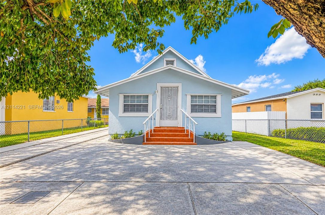 Gabled-roof exterior featuring a light blue stucco finish, front-facing concrete driveway, metal security screen door, and raised masonry steps