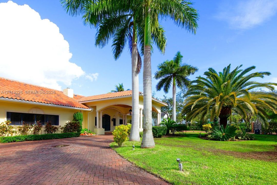Exterior featuring a terracotta tile roof, brick paver driveway, covered entryway with classical columns, and mature palm trees
