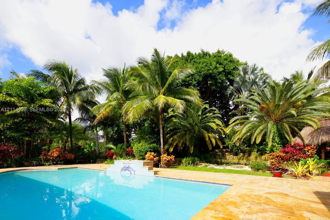 Swimming pool with a stone tile deck, a raised water feature, mature palm trees, and lush tropical landscaping