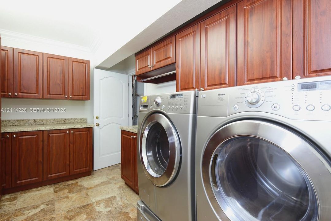 Laundry room featuring raised-panel wood cabinetry, stone-finish countertops, tile flooring, and crown molding