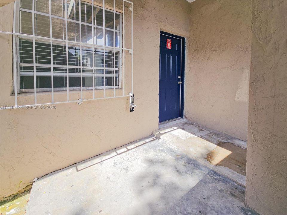Covered entryway featuring textured stucco exterior walls, a solid-panel door, and a window with exterior security bars
