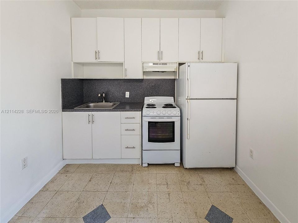 Kitchenette featuring white cabinetry, dark-toned countertop, stainless steel sink, white electric range, and white refrigerator