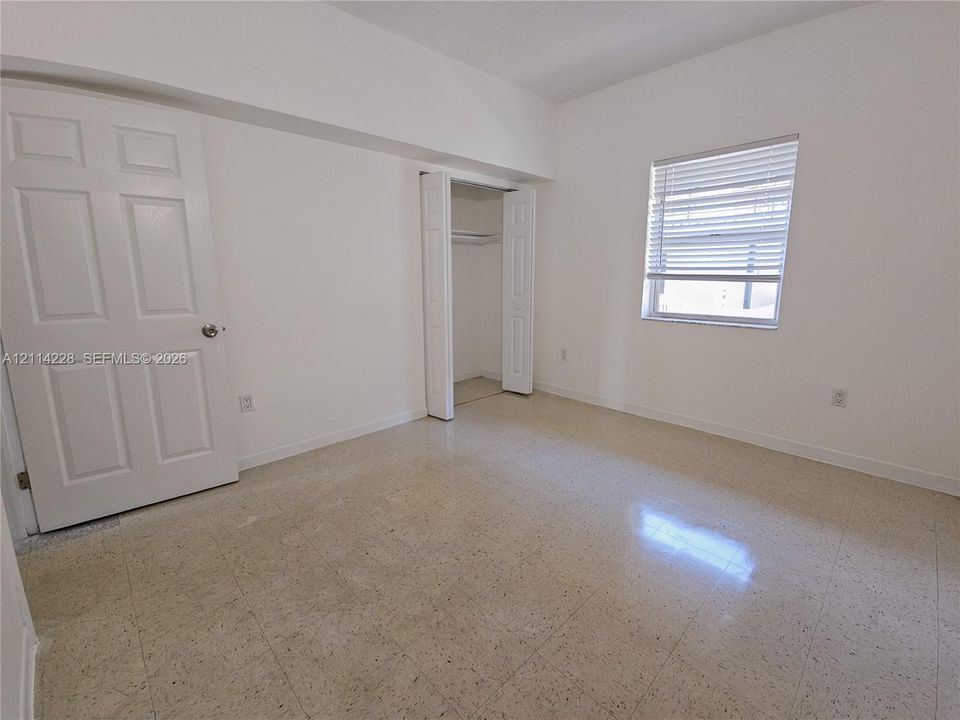 Neutral room featuring tile flooring, a single window with horizontal blinds, a six-panel door, and a built-in closet with bifold doors