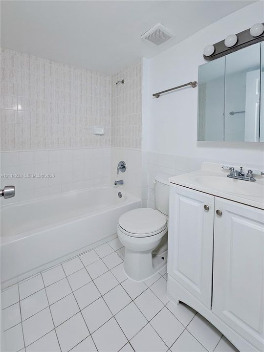Bathroom featuring a vanity with integrated sink, tri-panel mirrored medicine cabinet, tub-shower combination with ceramic tile surround, and tile flooring