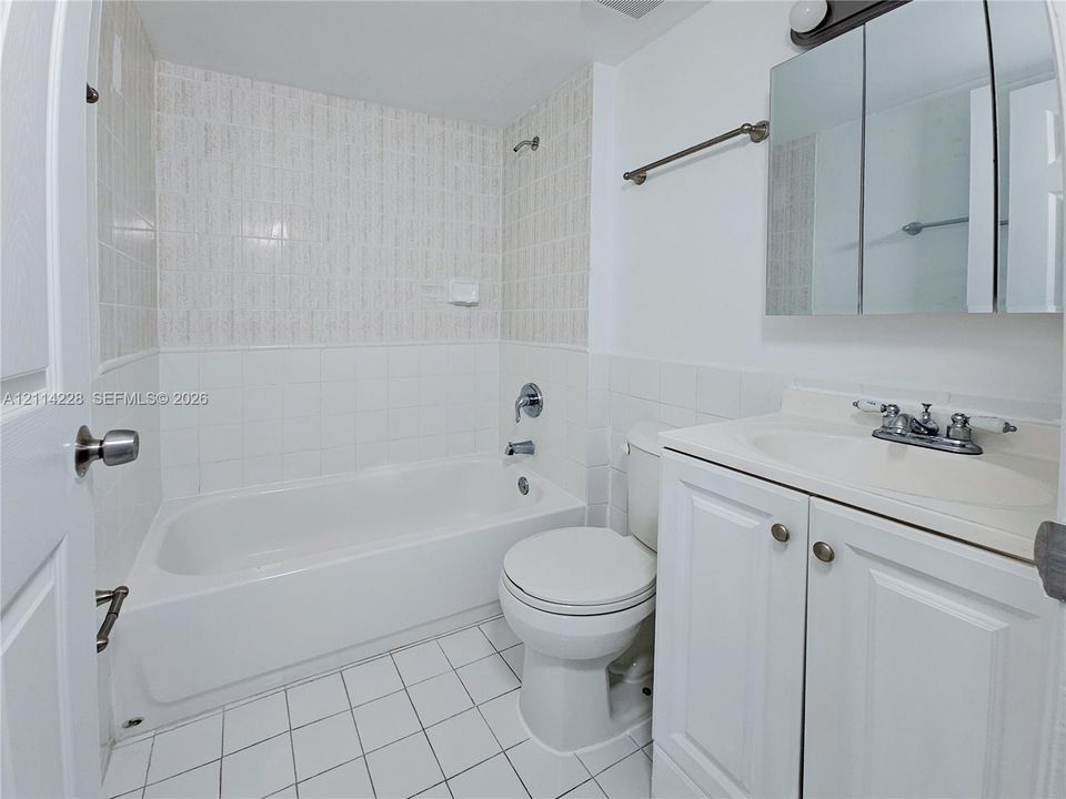 Bathroom featuring a porcelain tub with shower head, tiled wall surround, white vanity cabinet with a integrated sink, and triple-panel mirrored medicine cabinet