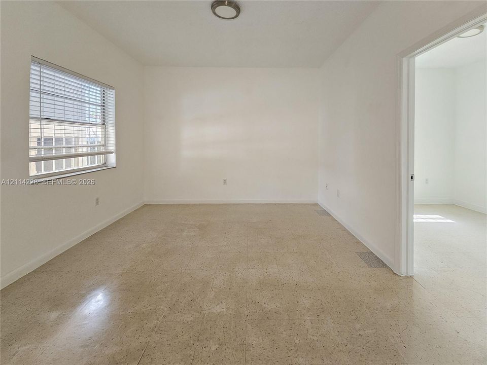 Neutral interior room featuring neutral-tone flooring, crisp white walls, a single-pane window with horizontal blinds, and a flush-mount ceiling light fixture