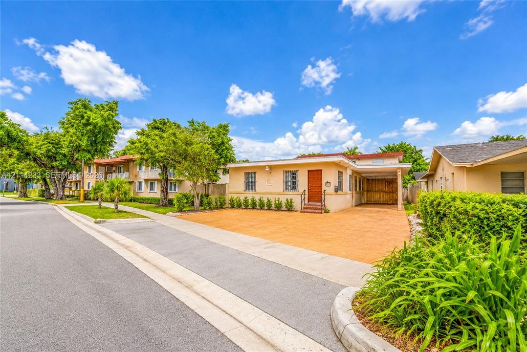Single-story residence featuring a stucco exterior, concrete-paved driveway, attached carport, and manicured landscaping