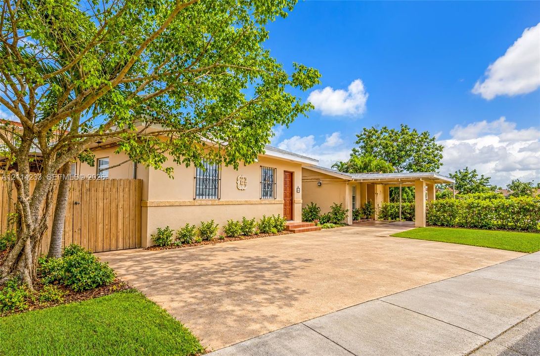 Stucco exterior featuring an expansive paved driveway, a covered front portico, privacy-style wood fencing, and window security bars