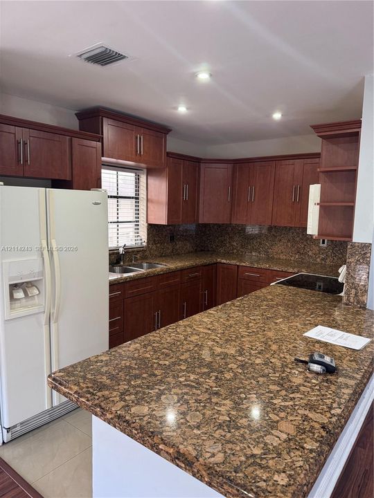 Kitchen featuring wood cabinetry, stone countertops, integrated recessed lighting, and a dual-basin stainless steel sink
