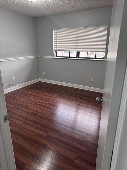 Room featuring wood-finish flooring, white chair rail molding, and a single-pane window with horizontal blinds