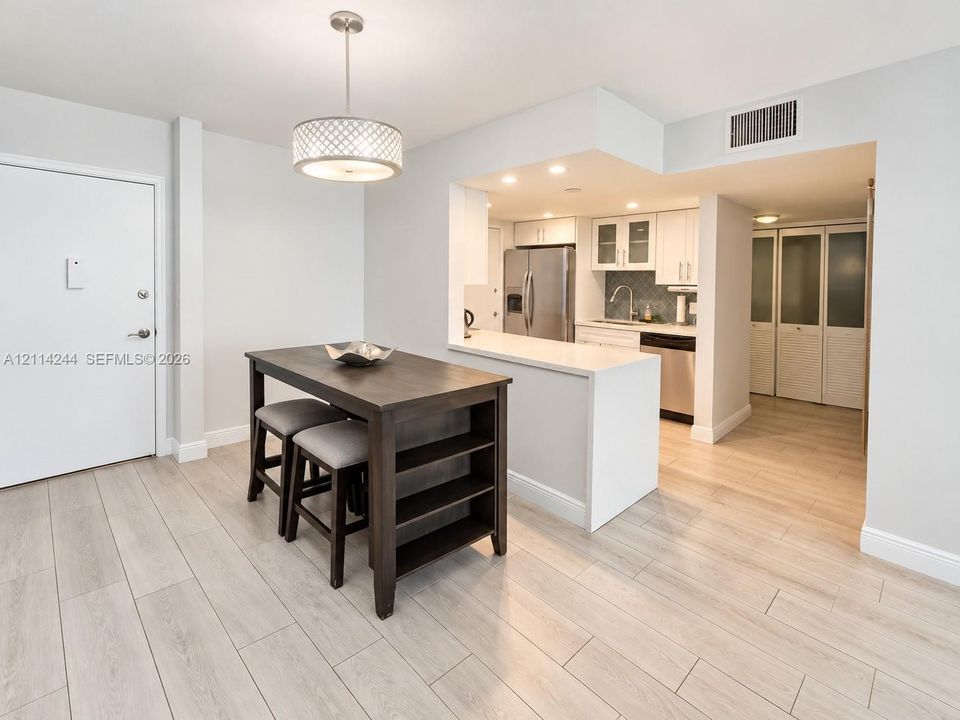 Dining and kitchen featuring quartz countertops, stainless steel appliances, white cabinetry.